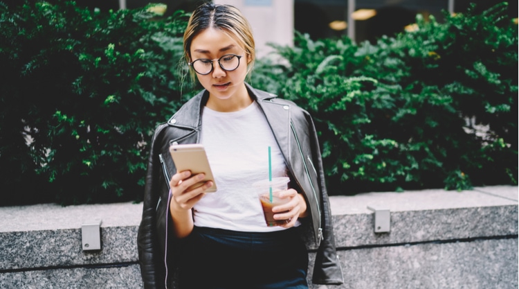 A young woman looking at her cell phone and standing outside