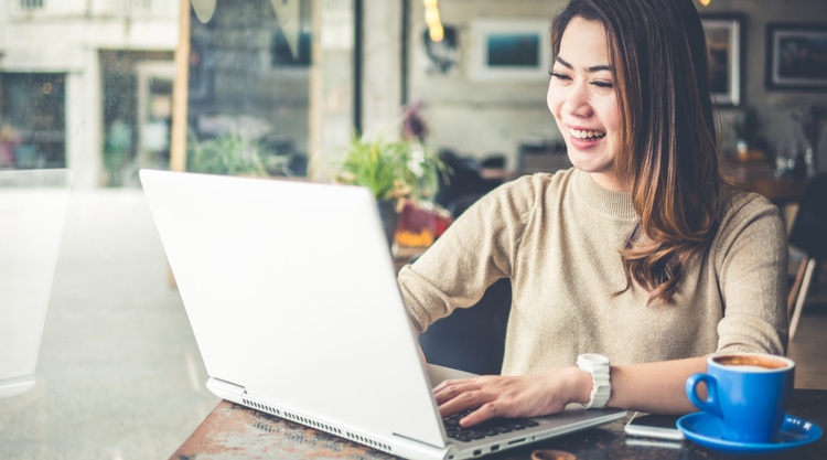 A smiling woman typing on her laptop and sitting in a cafe